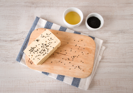 Fresh raw tofu on shabby cutting board with black cumin seeds and olive oilの写真素材
