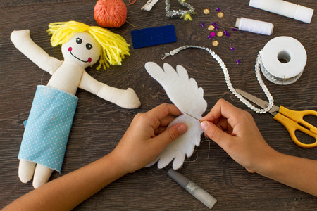 Child making a felt angel doll with sewing supplies on wooden table.の写真素材