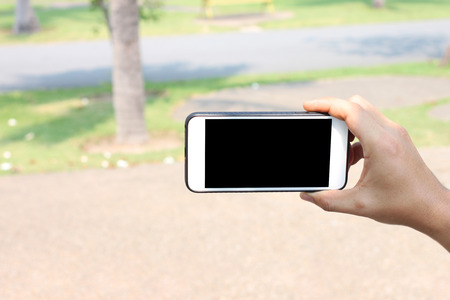 Hand of a man holding Smartphone for selfie in the garden and have Blank screen black for design in your work.の写真素材