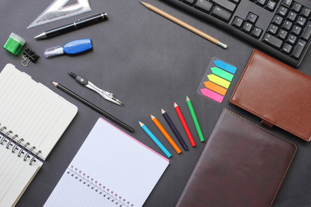 Top view notebook and pencil keyboard with accessories placed on a black desk in office and have...