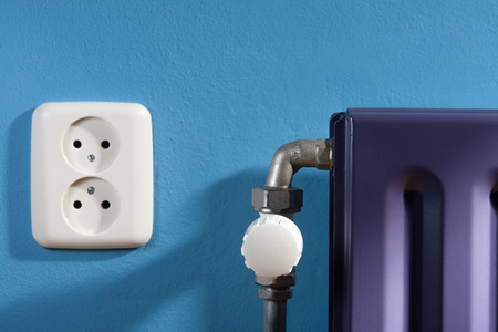 Thermostat on a purple central heating radiator and a blue wall with power pointの写真素材