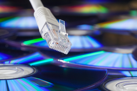 Close-up of a network plug and cable with a pile of cds technical background