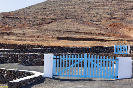 Volcanic stones and white concrete fence wall with blue wooden wicket gate typical on Lanzarote in Spainの写真素材