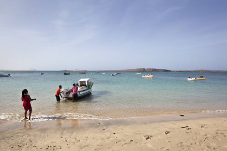 Sal Rei, Cape Verde ?? January 28, 2020: Two local men standing in the water near a small...