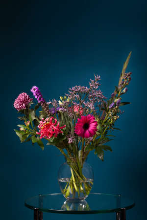Fresh bouquet of flowers in a glass vase on a glass table with a dark blue backgroundの写真素材