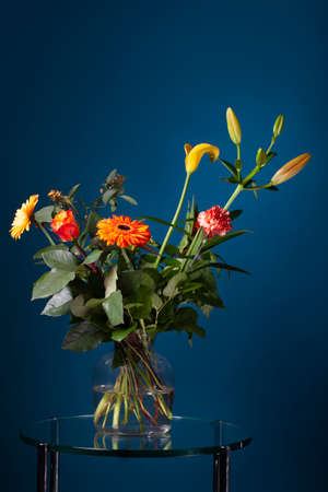 Fresh bouquet of flowers in a glass vase on a glass table with a dark blue backgroundの写真素材