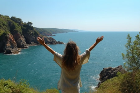 Young woman with arms outstretched looking at the sea from the top of the mountain with Generative AI.の素材