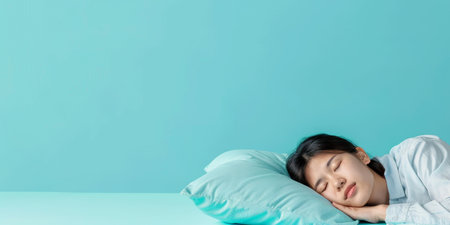 A young woman sleeping on a pillow. She is wearing a white shirt and has long black hair. The background is blue.の素材