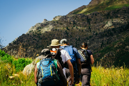 Group of hikers with backpacks walking towards the mountainsの写真素材