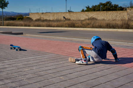 boy getting up after falling into a skateboarding accident. He is wearing helmet and protections and is lying at a bike lane.の写真素材