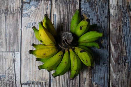 Fresh green bananas with a few turning yellow, placed on a weathered wood surface.の写真素材