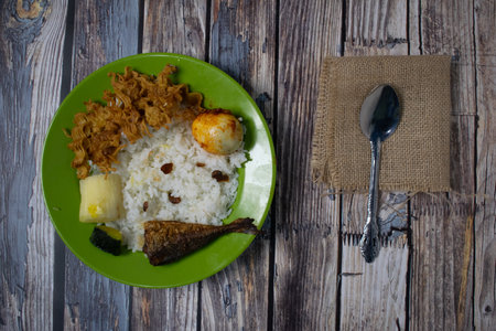 Traditional food served on a green plate with rice, egg noodles, boiled eggs, cassava, pumpkin and fried fish.の写真素材