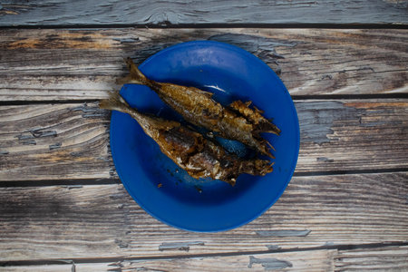 Traditional fried fish served on a vivid blue plate in rustic settingの写真素材