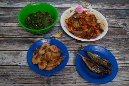 Traditional food with spicy shrimp, fried fish and stir-fried vegetables served on a rustic table.の写真素材