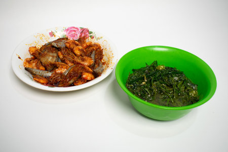 A dish featuring spicy shrimp and eggplant in a red sauce, served with green leafy vegetables.の写真素材