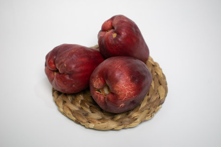 Three red Jamaican guavas are placed on a woven straw mat.