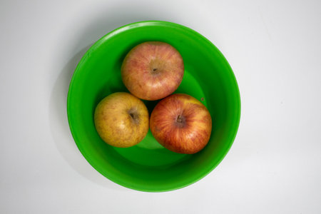 A green plastic bowl holding three red-yellow apples.の写真素材