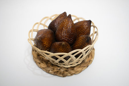Close-up of tropical snake fruit neatly arranged in a traditional bamboo basket on a white...