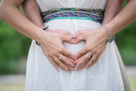 Image of parent's hands as a heart shape on bellyの写真素材