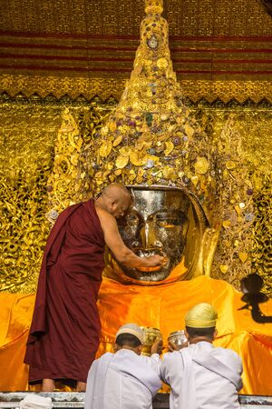 MANDALAY, MYANMAR - JUL 17, 2018 : Senior monk wash the face of Mahamuni Buddha image at Mahamuni temple. the most highly revered Buddha image in the country.のeditorial素材
