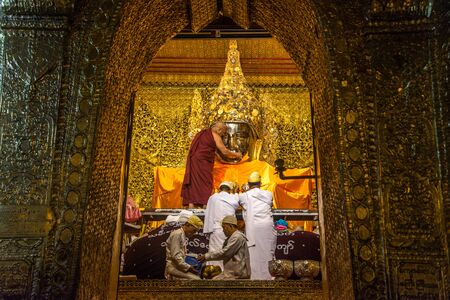 MANDALAY, MYANMAR - JUL 17, 2018 : Senior monk wash the face of Mahamuni Buddha image at Mahamuni temple. the most highly revered Buddha image in the country.のeditorial素材
