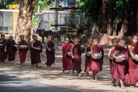BAGAN, MYANMAR - JUL 18, 2018: Buddhist novices walk to collect alms and offerings along the road at Bagan, Myanmar.のeditorial素材