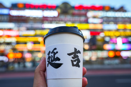 Hand holding cup wirh blur building on background, chinese alphabet means YANJI city in China.の写真素材