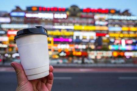 Hand holding cup wirh blur building on backgroundの写真素材