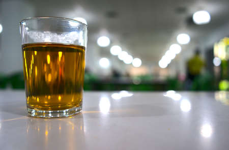 Hot tea drink with bokeh background. A cylinder glass of golden clear water beverage on table at...