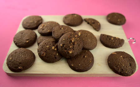 Dark baked chocolate cookies on wooden cutting board on pink acrylic background. Top view. Food photography, dessert, snack, cafe concept.の写真素材