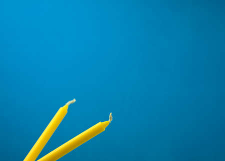 Bright yellow candles isolated on blue background. Off-center, head on, side view composition shot. Horizontal frame. Copy space.の写真素材