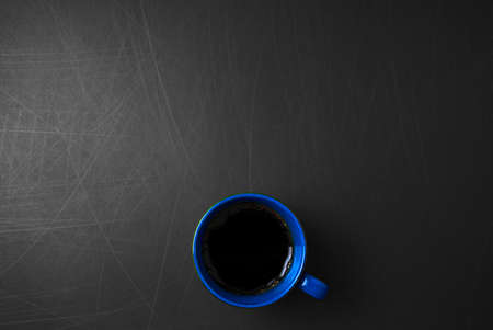 Blue ceramic cup of black hot coffee with golden foam on scratched grunge black background with copy space for your image or text. Off-center, horizontal image style.の写真素材