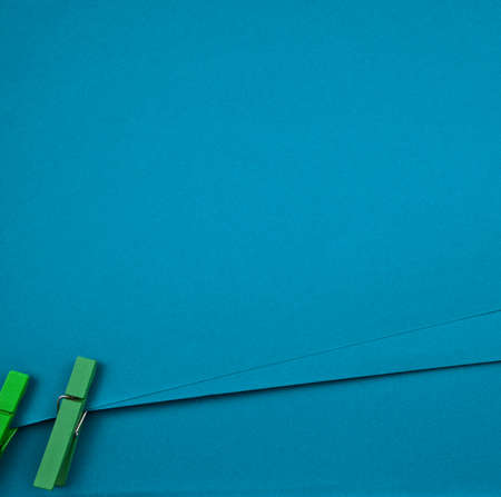 Blue blank paper texture abstract background. Binding with green wooden craft clips, pegs. Minimal design backdrop, display or memo concept. Free space for text, image or design. Overhead, vertical.の写真素材