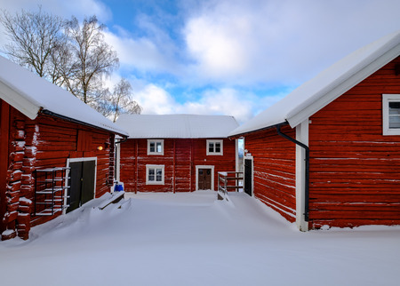 three red cottages with snow on the roofs and ground, blue sky with clouds in the backgroundの写真素材