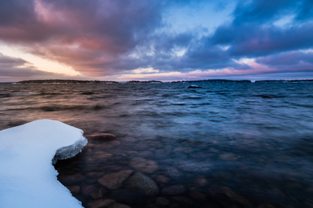 snow on rocks at the coast and sunset in the backgroundの写真素材