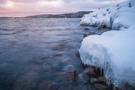 snow and ice on rocks at the coast and sunset in the backgroundの写真素材