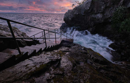 Stairs leading down to the sea with big waves and sunset in the background