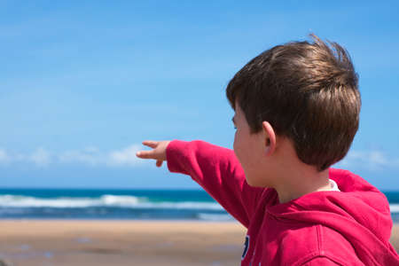 Child in red sweatshirt pointing to the sea on a clear dayの写真素材