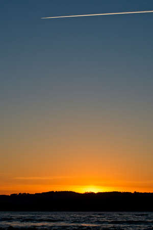 sunset on a hill with the sea in front with airplane steam trails at the top with clear skyeの写真素材
