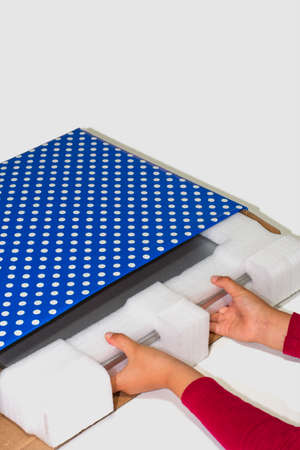 Red-sleeved kid unpacking a silver laptop gift-wrapped in blue wrapping paper with white circles and a white background.の写真素材