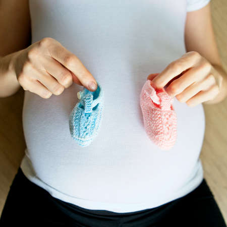 pregnant woman showing two booties on her belly, one blue and the other pink.の写真素材