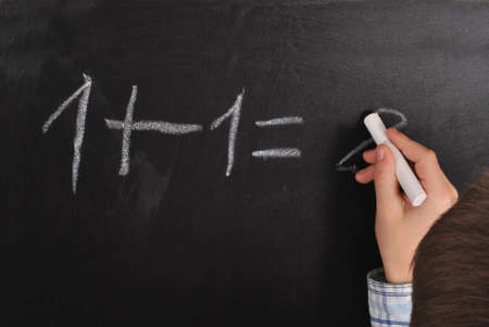 One plus one on blackboard- child is writing down the result  の写真素材