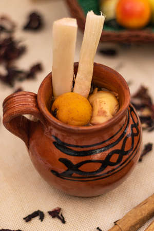 Traditional Mexican jug of Christmas fruit punch with cane, tejocote and guava. On the table, jute tablecloth, cinnamon and hibiscus leavesの写真素材
