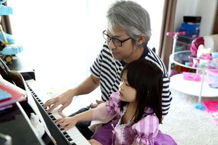 The Asian man teaching daughter to play piano.の写真素材