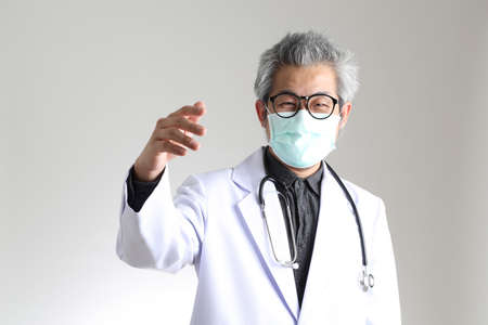 The senior Asian physician with mask on the white background.の写真素材