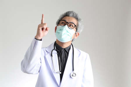 The senior Asian physician with mask on the white background.の写真素材