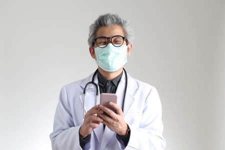 The senior Asian physician with mask on the white background.の写真素材