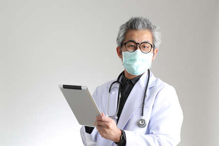 The senior Asian physician with mask on the white background.の写真素材
