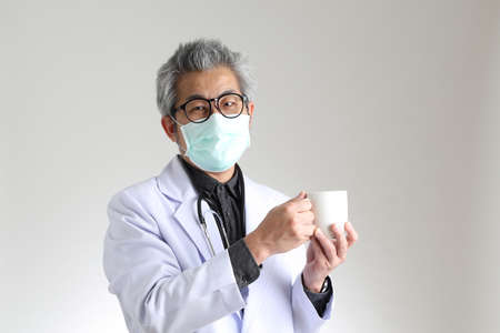 The senior Asian physician with mask on the white background.の写真素材
