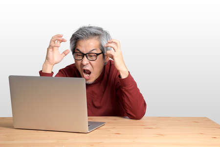 The Senior Asian man sitting at the desk on the white background.
